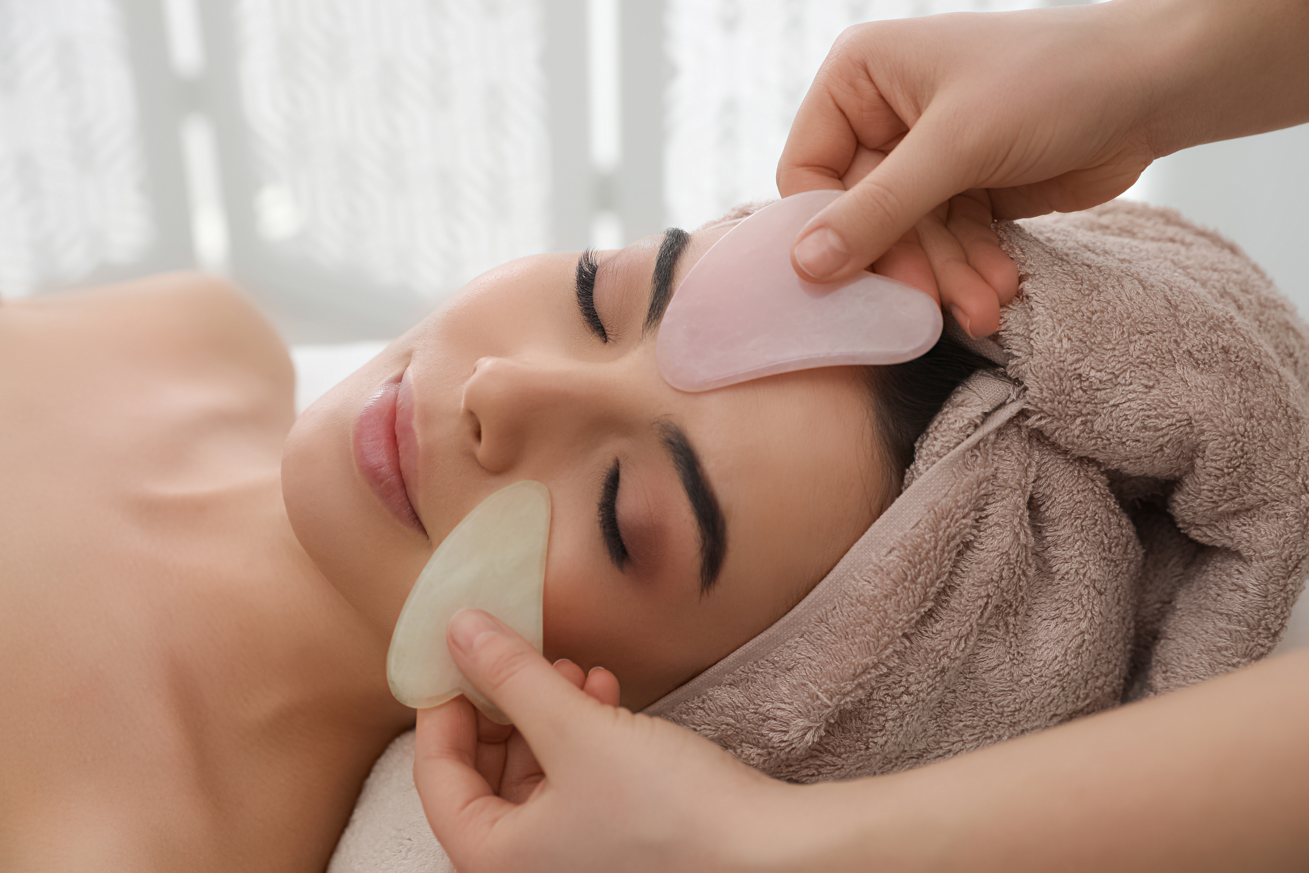 Young Woman Receiving Facial Massage with Gua Sha Tools in Beaut